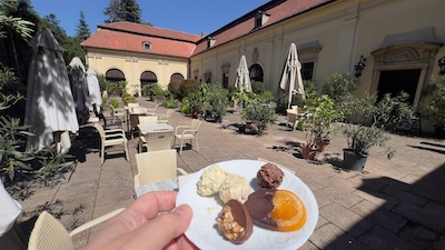 Ein Teller mit verschiedenen Schokoladebonbons, dahinter ein historischer Hof mit Kaffeehausbestuhlung.