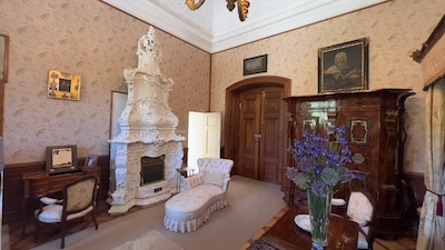 Ein Wohnraum mit einem großen weißen Barockofen, Barockschränken, davor eine Chaiselongue.