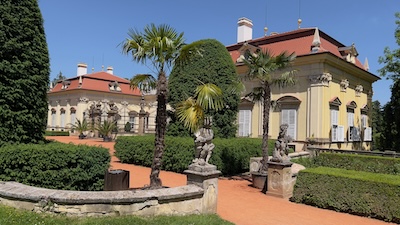 Ausgangsbereich des Hofes von Schloss Buchlovice zum Garten. Palmen, Barockfiguren, Hecken und eine gerundete Balustrade.