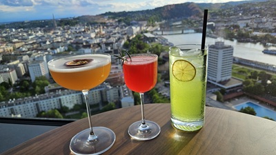 Drei Cocktails - orange, rot und grün vor der Skyline von Linz.