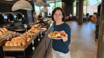 Frau mit Teller mit Gemüse und Aufstrichen vor dem Frühstücksbuffet im ARCOTEL Tabakfabrik.
