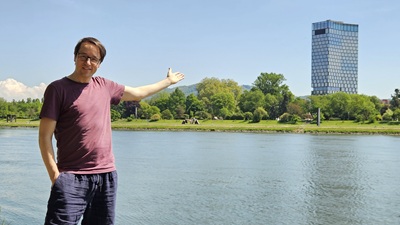 Mann zeigt vom anderen Donau-Ufer auf den Quadrill Tower in Linz mit dem ARCOTEL Tabakfabrik.