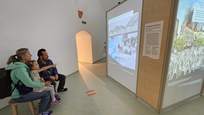 Eltern mit Kind sehen ein auf eine Wand projeziertes Video über die Geschichte von Flüssen.