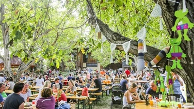 Menschen sitzen bei Holztischen im Garten beim ADAMAH BioHof-Fest