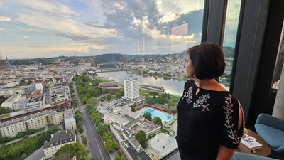 Frau blickt vor Glasfront vom Q27 hinunter auf Linz und die Donau.