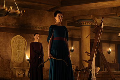 Anne Hathaway als Königin Penelope starrt auf ihre Freier, an ihrer Seite Mia Goth als die Bedienstete Melantho im Film Die Odyssey