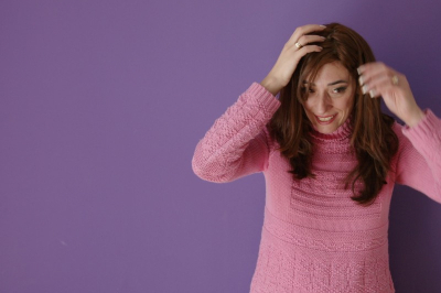 Brünette Frau mit Perücke in rosa Pulli vor violettem Hintergrund..Foto der aktuellen Sommer-Ausstellung im Jüdischen Museum Dorotheergasse