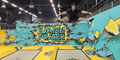 Man springt auf einem Trampolin, die Beine und Arme auf die Seite gestreckt, bei Jumpin Prater in Wien.
