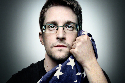 Dunkelblonder Mann mit Brille hält die US-Flagge an sein Gesicht, Blick nach vorne gerichtet