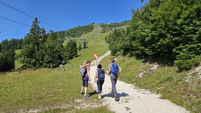 Drei Wanderer am Escape Trail der Gemeindealpe auf Höhe Mittelstation mit Blick auf den Sessellift und das Terzerhaus