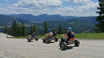Familie auf drei Mountaincarts auf der Gemeindalpe mit Blick auf das Bergpanorama.