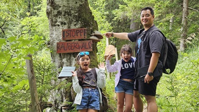 Vater mit Kindern zeigt auf Baum mit Räuberwald-Schild bei Katta und der Räuberwald