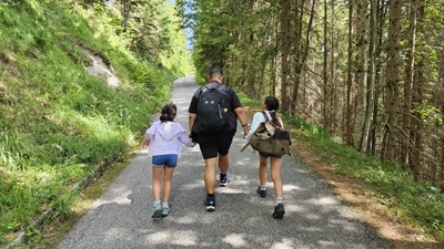 Vater mit zwei Töchtern geht einen Asphaltweg durch den Wald hinauf.