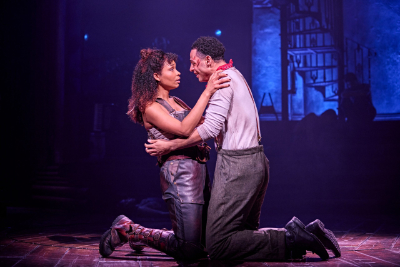 Eine junge schwarze Frau und ein junger schwarzer Mann knien am Boden und halten sich in den Armen im Musical Hadestown