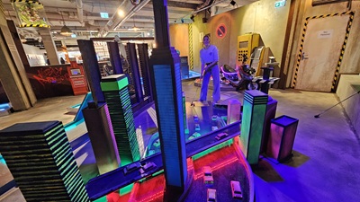 Frau spielt auf einer Minigolfbahn mit beleuchteten Hochhausmodellen