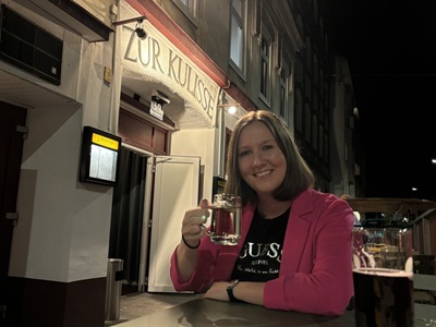 "Helden"-Redakteurin Stefanie Riegler trinkt einen Spritzer im Gastgarten vor der Kulisse.