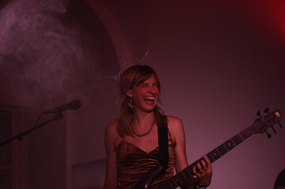 Anna Grob mit ihrem Bass steht auf der Bühne im Perchtlsaal beim Popfest und lacht.