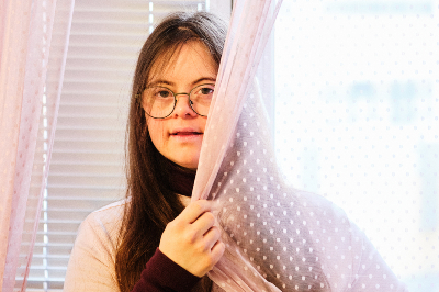Frau mit langen braunen Haaren und Brille, umhüllt das Gesicht teilweise mit einem Vorhang